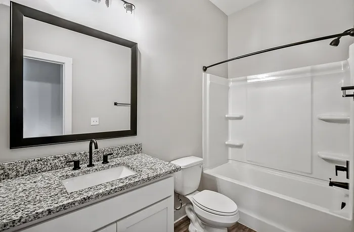 Modern bathroom featuring sleek granite countertops, large framed mirror, and pristine bathtub with contemporary fixtures.