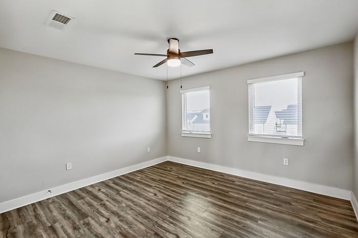 Bright and inviting empty room with elegant wood flooring and a sleek ceiling fan, perfect for personal touches.