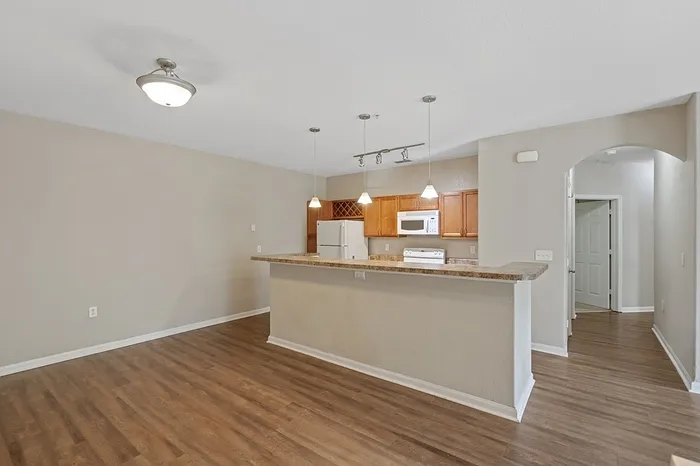 Contemporary open-plan kitchen with sleek wooden flooring, elegant pendant lighting, and stylish cabinetry perfect for modern living.