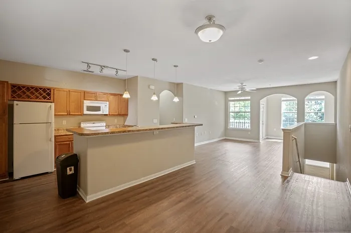 Bright and airy open-concept living area with hardwood floors, modern kitchen island, and large windows overlooking lush greenery.