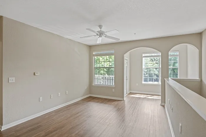 Bright and airy living space with hardwood floors, large windows, and elegant archways offering a charming view.