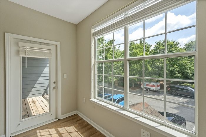 Bright apartment view featuring large windows with a serene and leafy outlook, hardwood flooring, and a cozy balcony for relaxing.