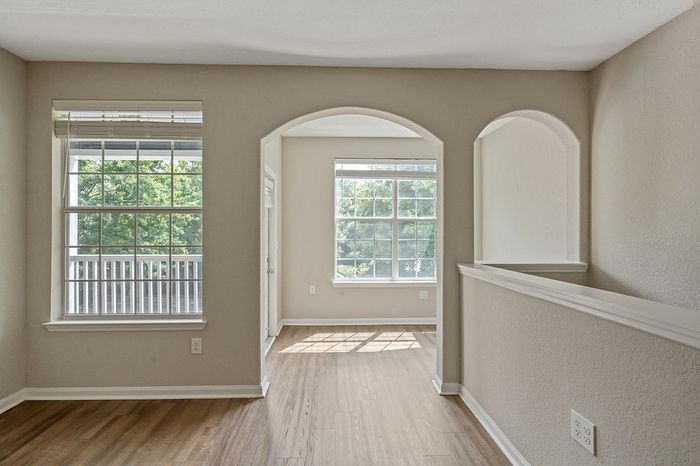 Bright and inviting living space with large windows, elegant archway, and warm wood flooring.