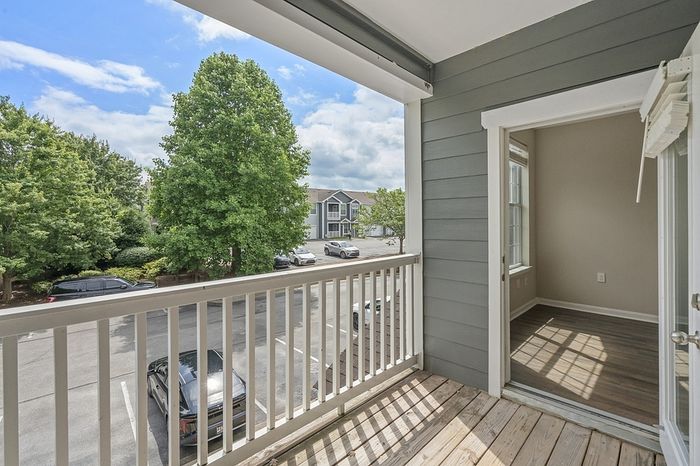 Charming apartment balcony with serene tree-lined views and sunlit entryway.