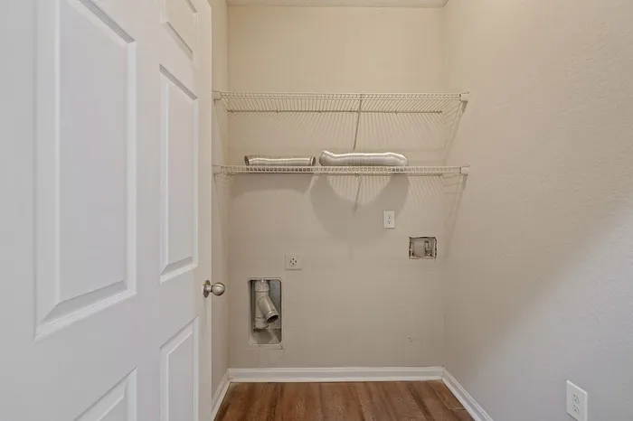 Bright utility room with modern shelving, ready for washer and dryer installation, featuring warm wood flooring.