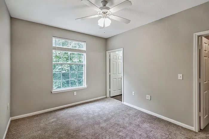 Bright bedroom with soft carpeting, large window offering lush green views, and a ceiling fan for added comfort.