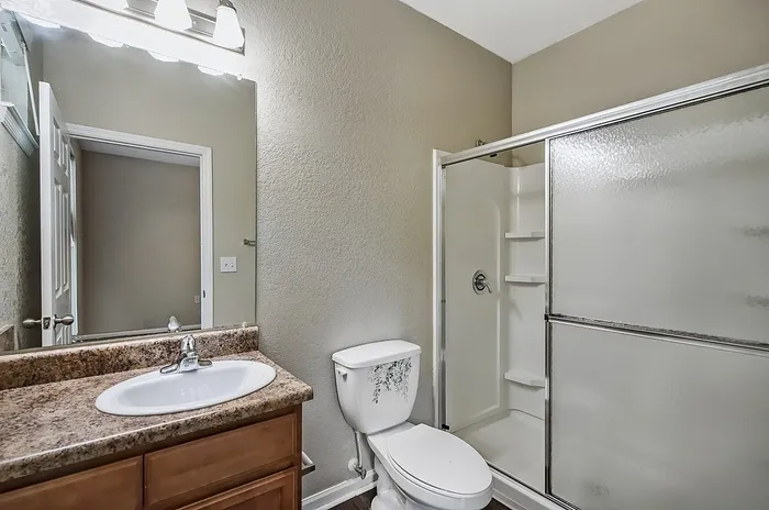 Bright and modern bathroom featuring a sleek shower with glass doors, elegant granite countertop, and clean vanity lighting.