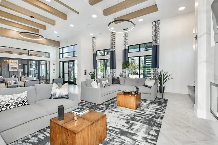 Luxurious open-concept living room with sleek gray sofas and modern decor, featuring high ceilings and elegant lighting.
