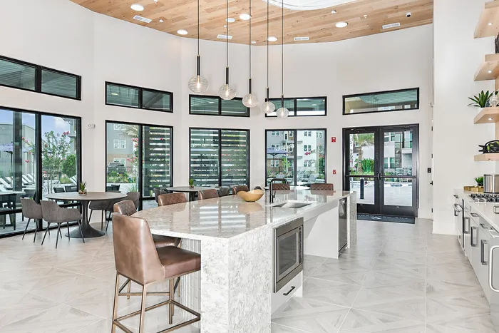 Modern, sunlit kitchen and dining area with elegant marble countertops, stylish pendant lights, and expansive windows offering a view of the landscaped outdoor space.