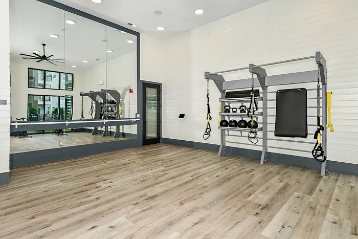 Modern fitness studio with sleek wooden flooring, mirrored wall, and essential workout equipment including TRX bands and kettlebells.