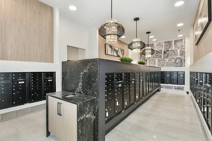 Modern apartment mailroom with chic lighting, sleek black mailboxes, and contemporary wall art, offering a welcoming entrance.