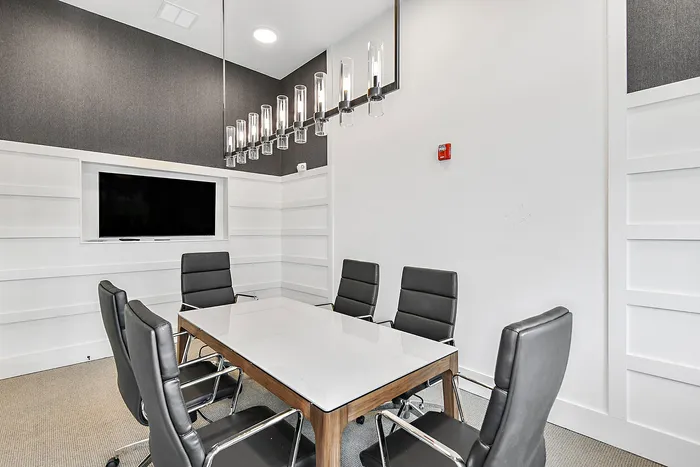 Modern conference room featuring sleek chairs around a polished marble table, elegant lighting fixtures, and a mounted TV for presentations.