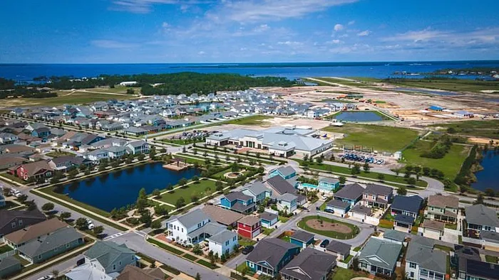 Vibrant aerial view of a picturesque coastal neighborhood featuring modern homes, lush greenery, and serene water bodies under a bright blue sky.