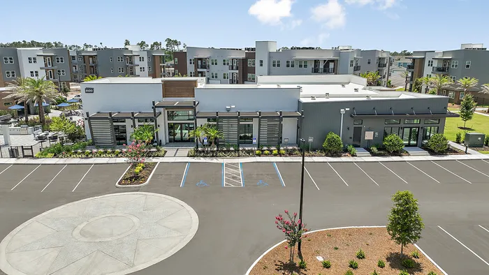 Chic modern apartment complex featuring clean architectural lines, lush landscaping, and ample parking, set against a beautiful blue sky.