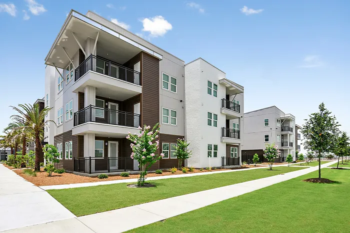 Modern apartment complex with stylish balconies and lush green landscaping under a bright blue sky.