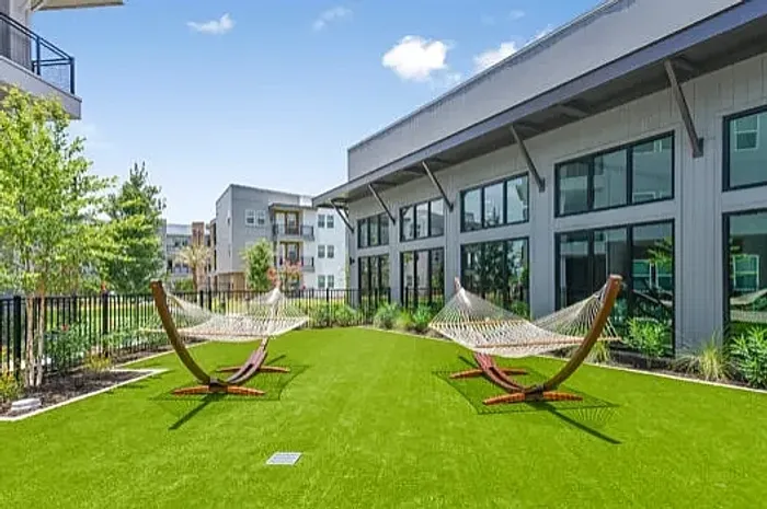 Elegant three-story apartment building featuring modern balconies and lush landscaping with a nearby putting green, set against a clear blue sky.