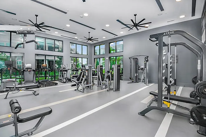Modern fitness center with state-of-the-art gym equipment, spacious layout, and large windows overlooking lush greenery.