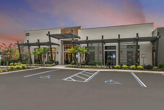 Elegant building exterior with modern architectural design, lush landscaping, and ample parking at sunset.