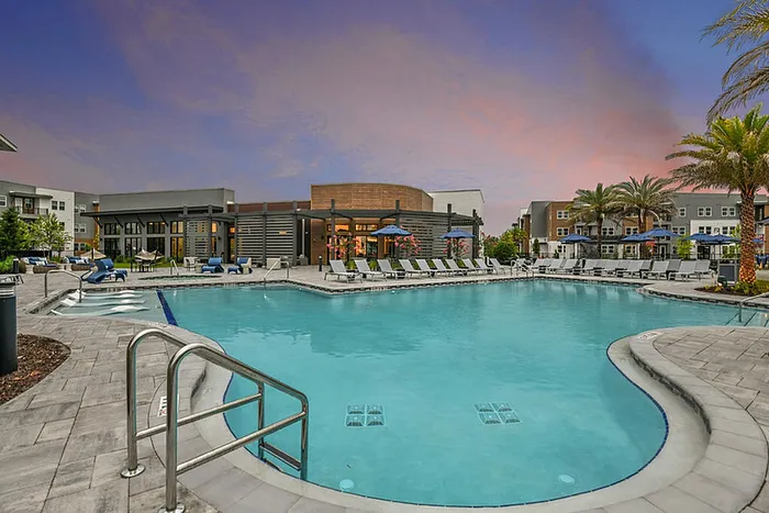 Luxurious apartment complex showcasing a stunning resort-style pool surrounded by contemporary buildings and lush palm trees under a picturesque sky.