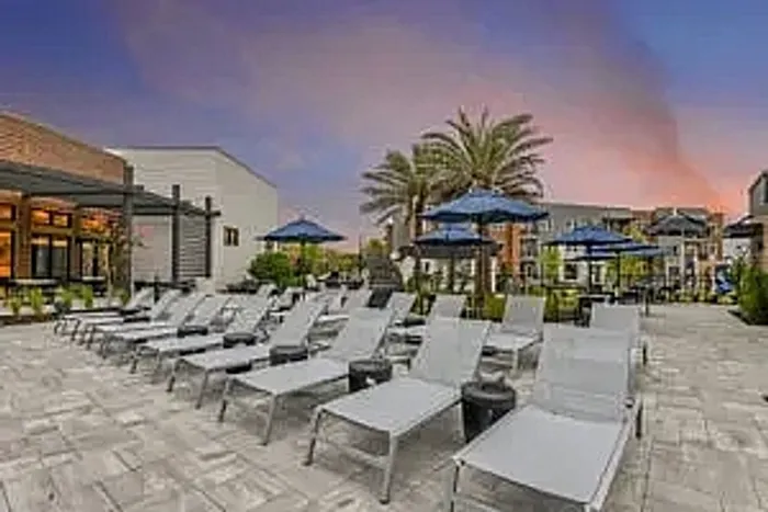 Luxurious apartment complex showcasing a stunning resort-style pool surrounded by contemporary buildings and lush palm trees under a picturesque sky.
