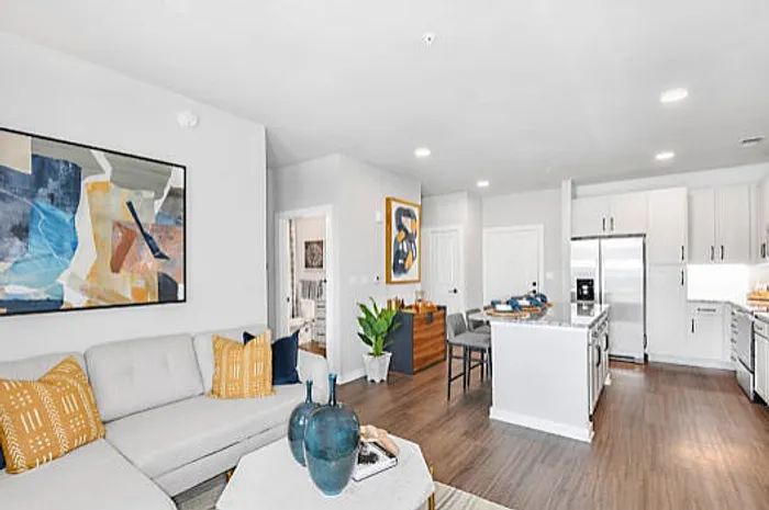 Modern open-concept living area with stylish decor, featuring a cozy sofa, vibrant artwork, and a sleek kitchen with stainless steel appliances.