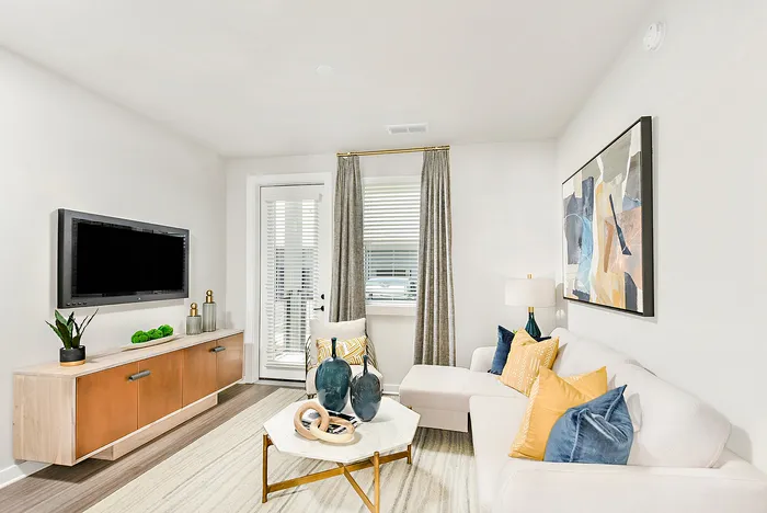 Bright and inviting modern living room with stylish decor, featuring a sleek white sofa adorned with colorful cushions, a chic marble coffee table, abstract wall art, and a large flat-screen TV.