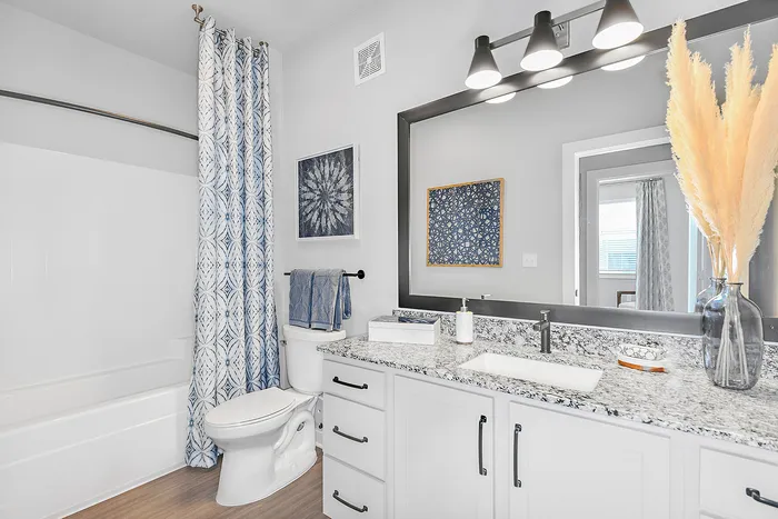 Elegant bathroom design featuring a granite countertop, chic blue patterned shower curtain, and stylish decor accents.