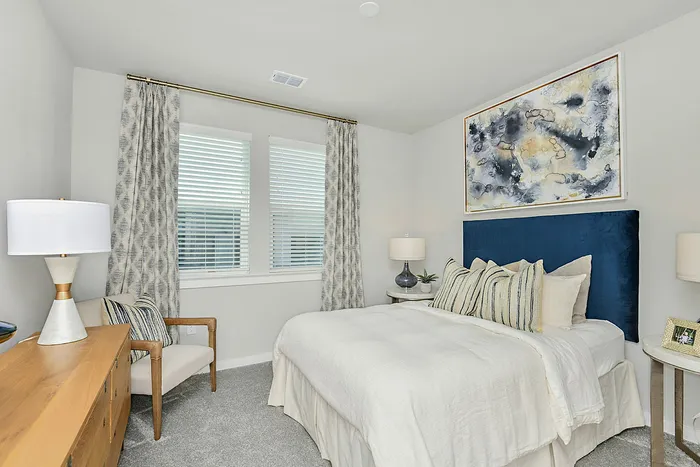 Chic, serene bedroom with a plush blue headboard, soft lighting, and elegant abstract artwork. Natural light filters through stylish curtains, enhancing the cozy, modern ambiance.