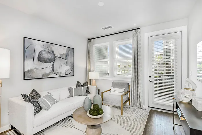 Elegant living room with contemporary decor, featuring a chic gray couch, modern art, and ample natural light through large windows.