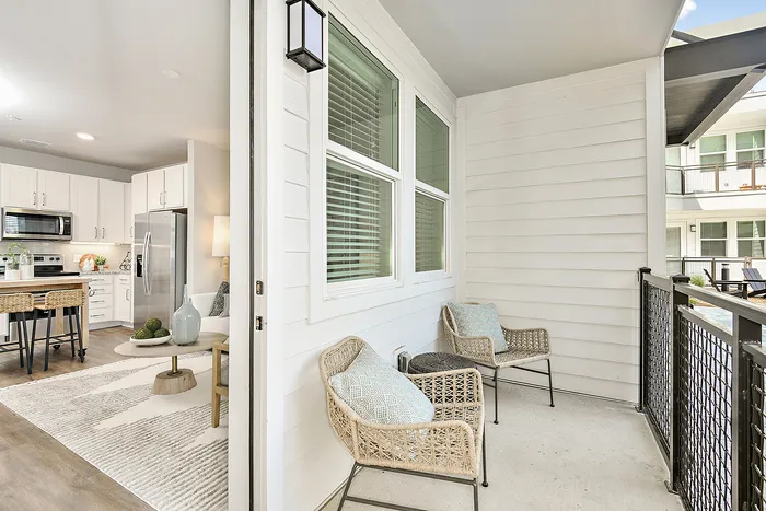 Inviting balcony with stylish wicker chairs overlooks modern interior featuring a sleek kitchen and cozy living area, perfect for relaxation and entertaining.