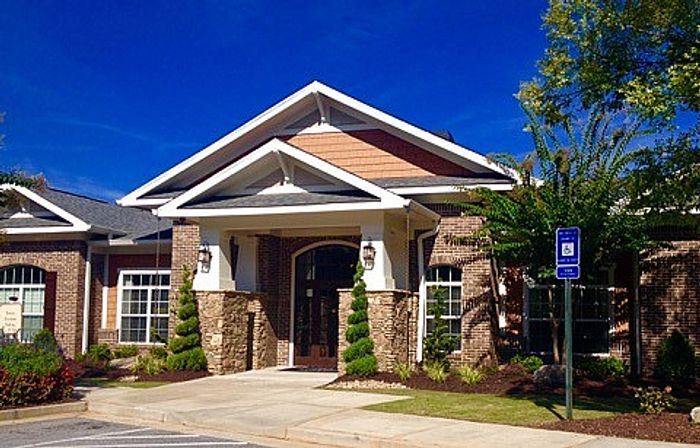 Charming brick-front building with a welcoming entrance, nestled amidst lush landscaping under a clear blue sky.