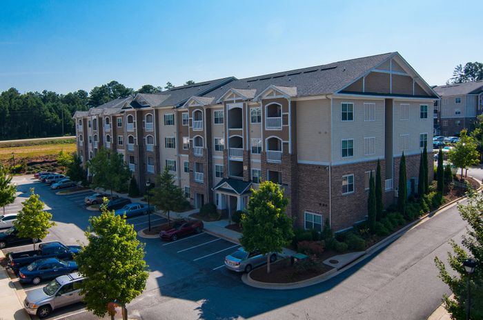 Beautiful multi-story apartment complex with modern architecture, surrounded by lush greenery and ample parking space.