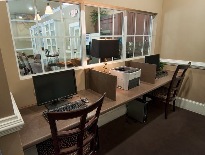 Modern business center featuring dual computer workstations, comfortable seating, and a window view into a welcoming lounge.