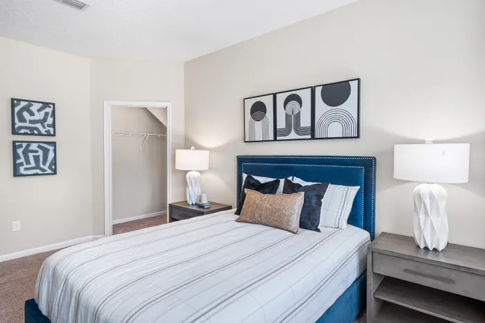Inviting bedroom featuring a plush blue headboard, modern abstract wall art, elegant side lamps, and a spacious closet.
