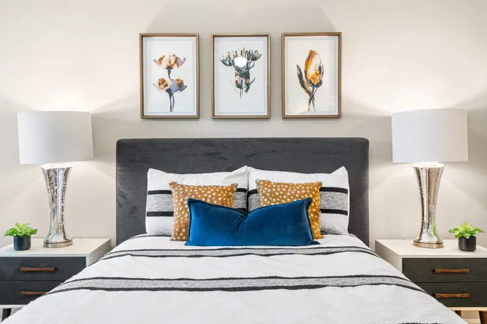 Elegant bedroom featuring a plush bed with patterned pillows, modern lamps on sleek bedside tables, and tasteful floral artwork.