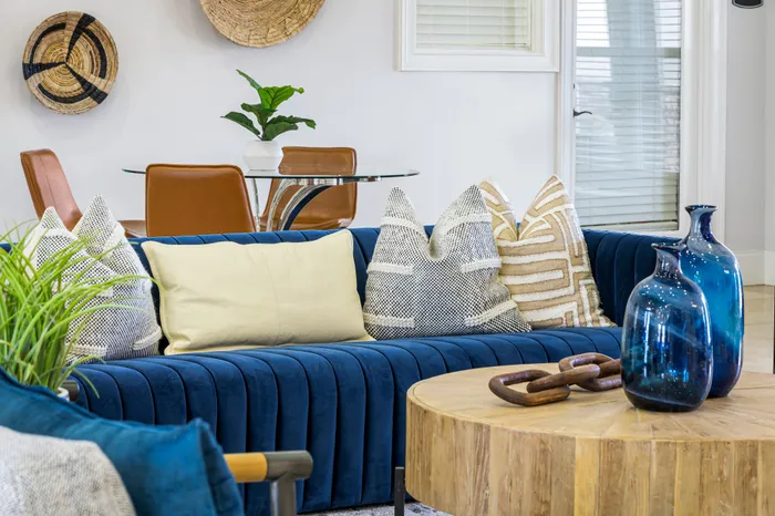 Chic and modern living room featuring a luxurious blue velvet sofa with stylish cushions, a wooden coffee table adorned with elegant blue vases, and a contemporary dining area with leather chairs.