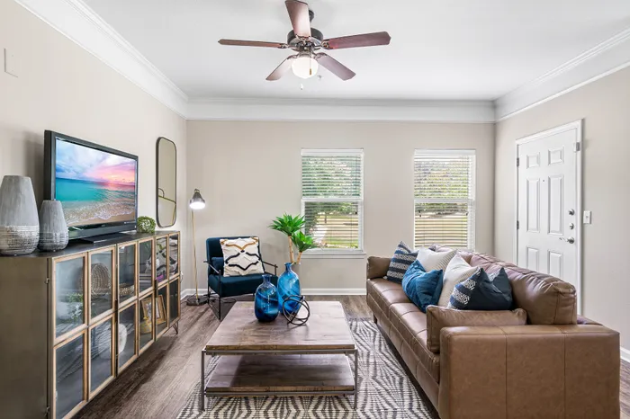 Bright and inviting living room with modern decor, featuring a comfortable leather sofa, stylish coffee table, and a flat-screen TV, enhanced by natural light from large windows.