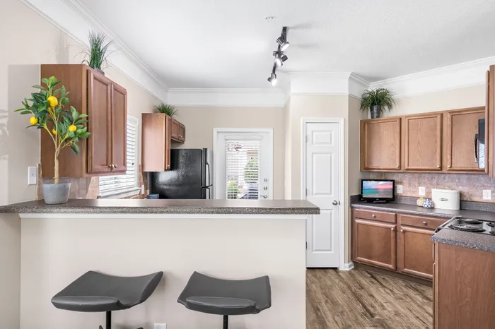 Modern kitchen with sleek countertops, wooden cabinets, and stylish bar stools, illuminated by elegant track lighting.