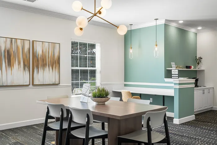 Modern dining area with sleek decor, featuring a stylish chandelier, contemporary artwork, and a cozy workspace with mint green accent wall.