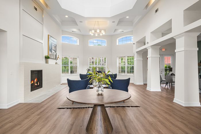 Elegant modern living room with high ceilings, large windows, and a cozy fireplace, featuring stylish blue chairs and a wooden center table.