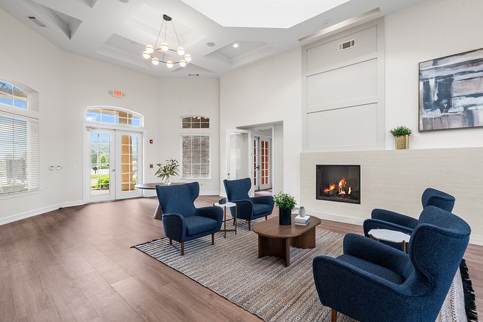 Elegant living room with high ceilings, modern chandelier, cozy fireplace, and stylish blue seating arrangements on wooden flooring.
