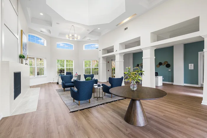 Elegant apartment lounge with high ceilings, modern blue armchairs, and large windows offering abundant natural light.