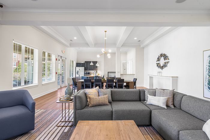 Spacious open-concept living room with elegant gray sofa, modern chandelier, and bright dining area leading to a sleek kitchen.