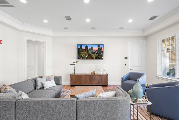 Elegant living room with modern gray sectional and blue armchairs, featuring a wall-mounted TV and stylish decor.
