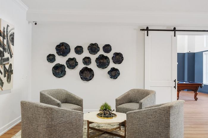 Elegant living space featuring modern gray chairs and a minimalist marble table, complemented by artistic wall decor and a sleek sliding door revealing a stylish billiard area.