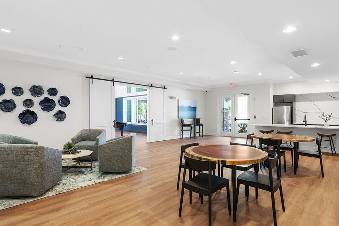 Elegant apartment lounge with modern decor, featuring cozy seating, round wooden tables, and a stylish open kitchen.