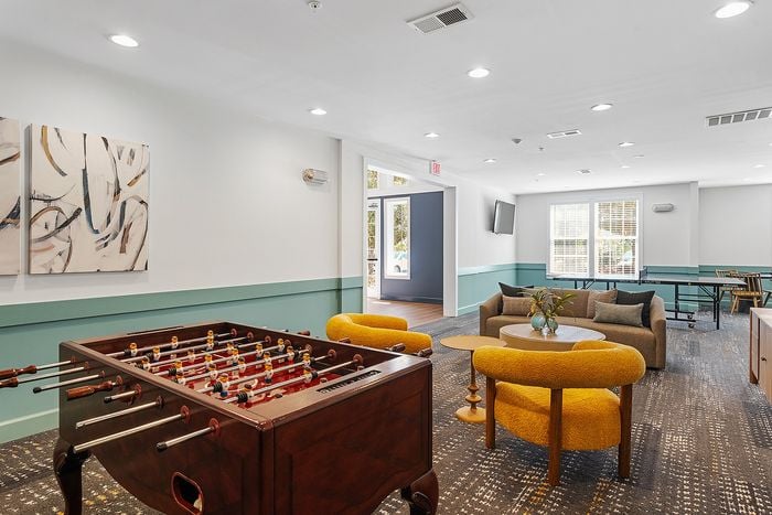 Bright and inviting communal lounge with modern decor, featuring a foosball table and cozy seating area.