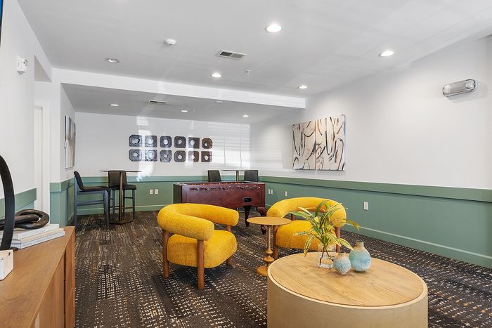 Chic and modern lounge with vibrant yellow chairs, elegant artwork, and a foosball table, perfect for relaxation and entertainment.