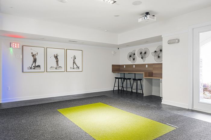 Modern recreational room featuring stylish golf-themed artwork, sleek bar seating, and a vibrant putting green area under bright lighting.