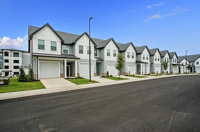 Charming row of modern townhouses with pristine white facades, spacious driveways, and lush green lawns under a bright blue sky.